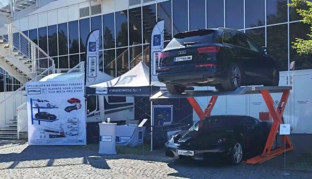 SYRISON 2.7-ton scissor parking lift showcasing structural rigidity with an Audi Q7 and Ferrari at a European automotive exhibition.